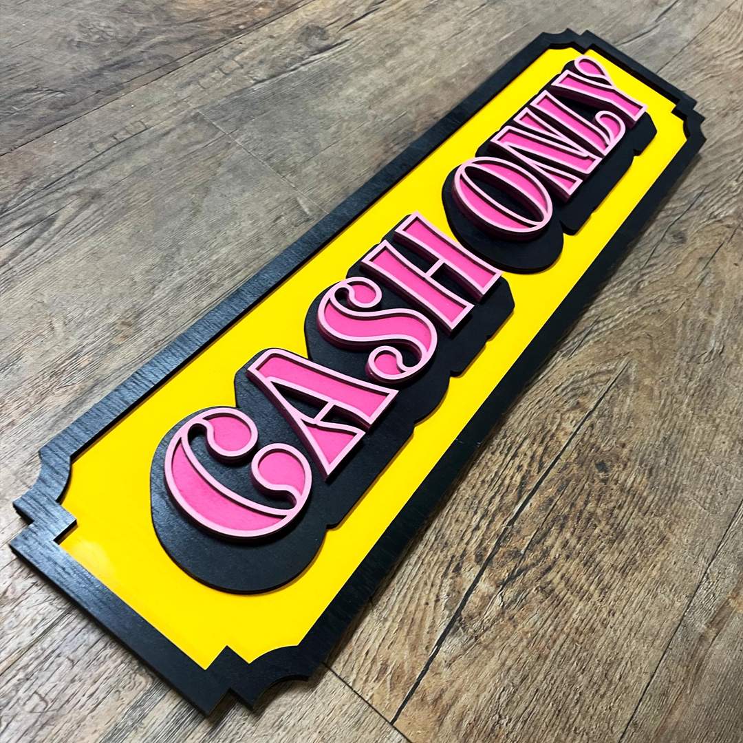 "Cash Only" bord van gelaagd hout met een retro design in roze, geel en zwart in tattoo shop.