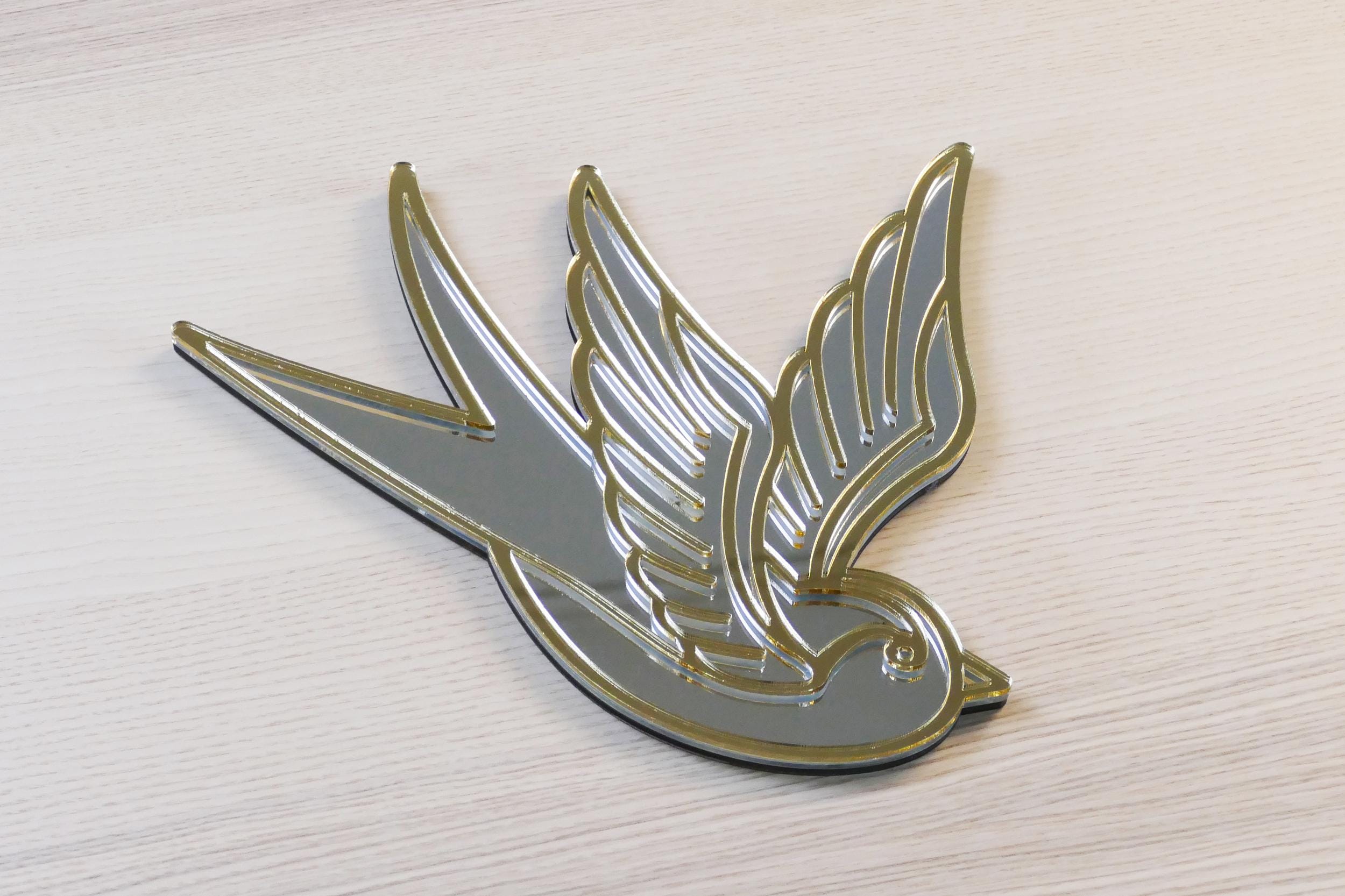 Gouden en zilveren acryl spiegel in tattoo-stijl van een zwaluw, hangend aan een muur.