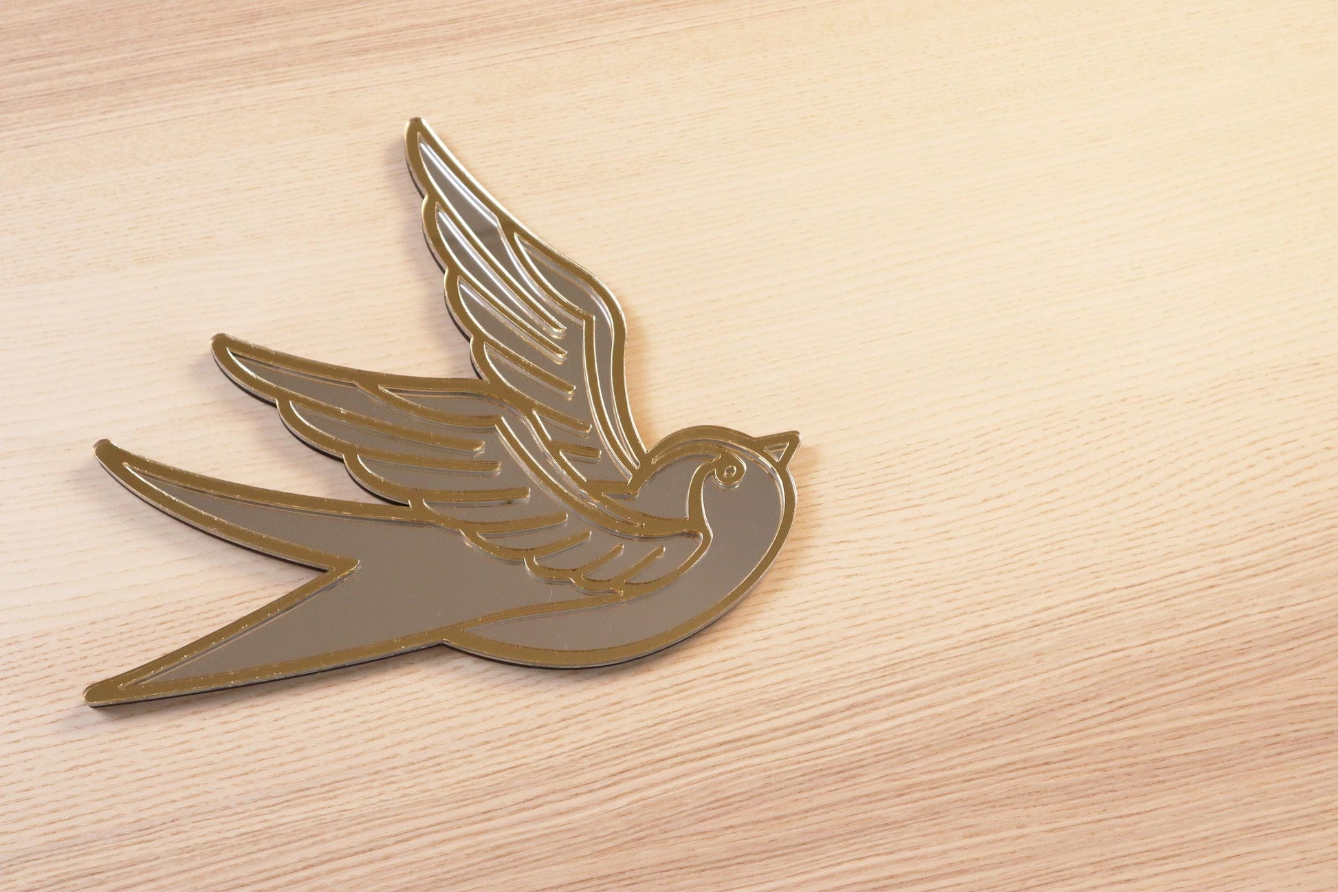 Gouden en zilveren acryl spiegel in tattoo-stijl van een zwaluw, hangend aan een muur. 