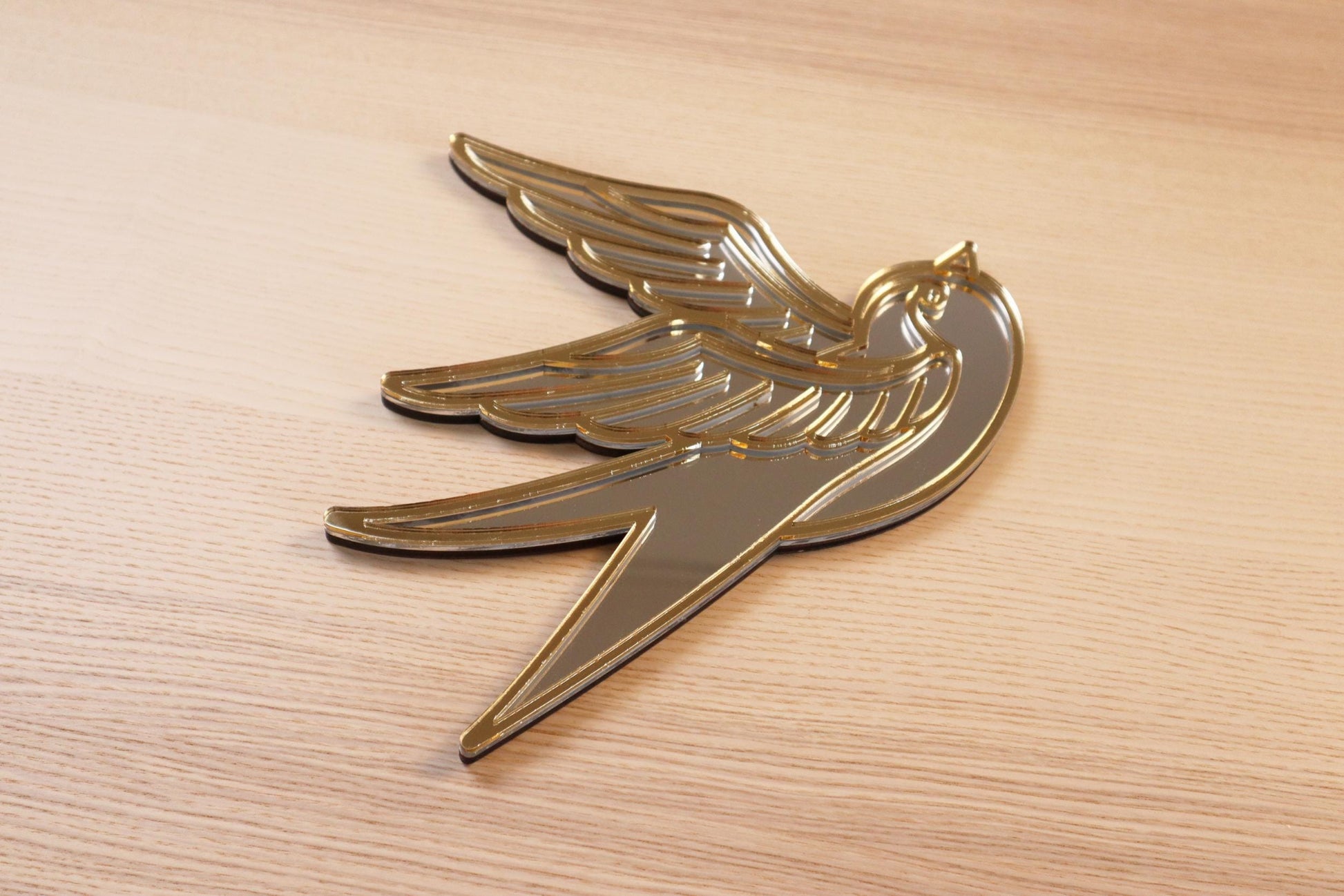 Gouden en zilveren acryl spiegel in tattoo-stijl van een zwaluw, hangend aan een muur.