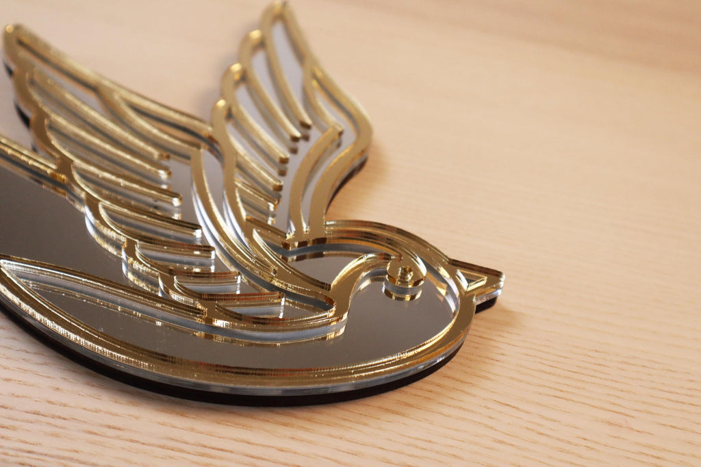 Gouden en zilveren acryl spiegel in tattoo-stijl van een zwaluw, hangend aan een muur. 
