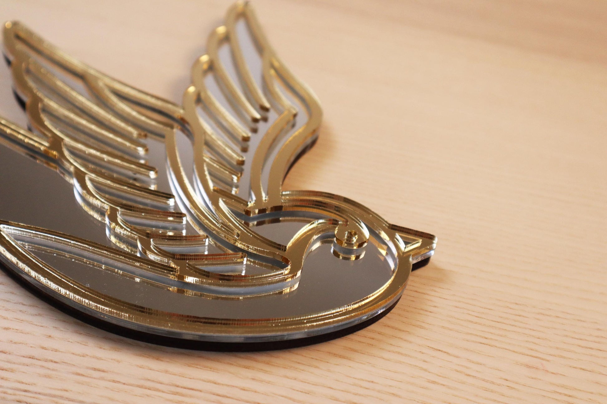 Gouden en zilveren acryl spiegel in tattoo-stijl van een zwaluw, hangend aan een muur. 
