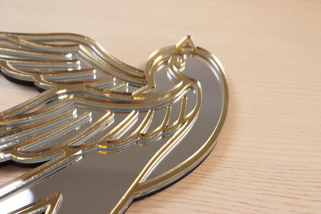 Gouden en zilveren acryl spiegel in tattoo-stijl van een zwaluw, hangend aan een muur.