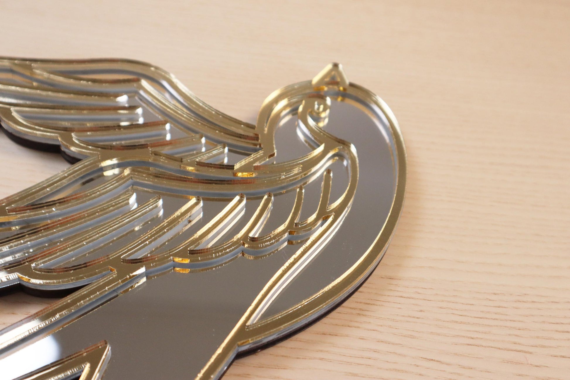 Gouden en zilveren acryl spiegel in tattoo-stijl van een zwaluw, hangend aan een muur.