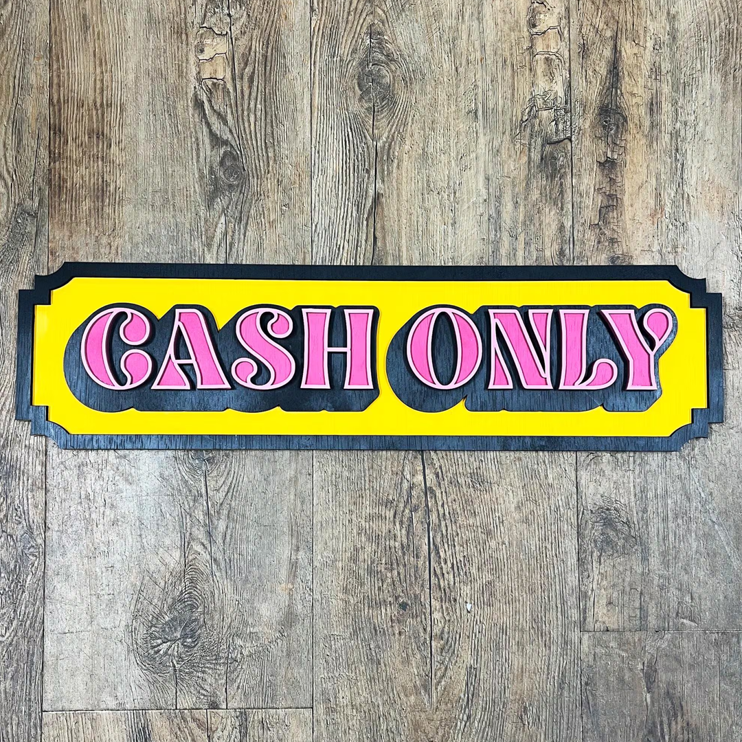 "Cash Only" bord van gelaagd hout met een retro design in roze, geel en zwart in tattoo shop.