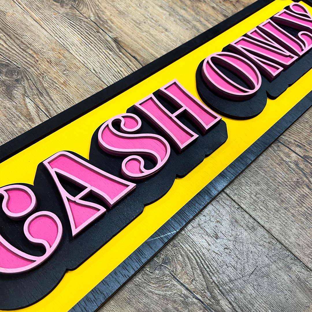 "Cash Only" bord van gelaagd hout met een retro design in roze, geel en zwart in tattoo shop.