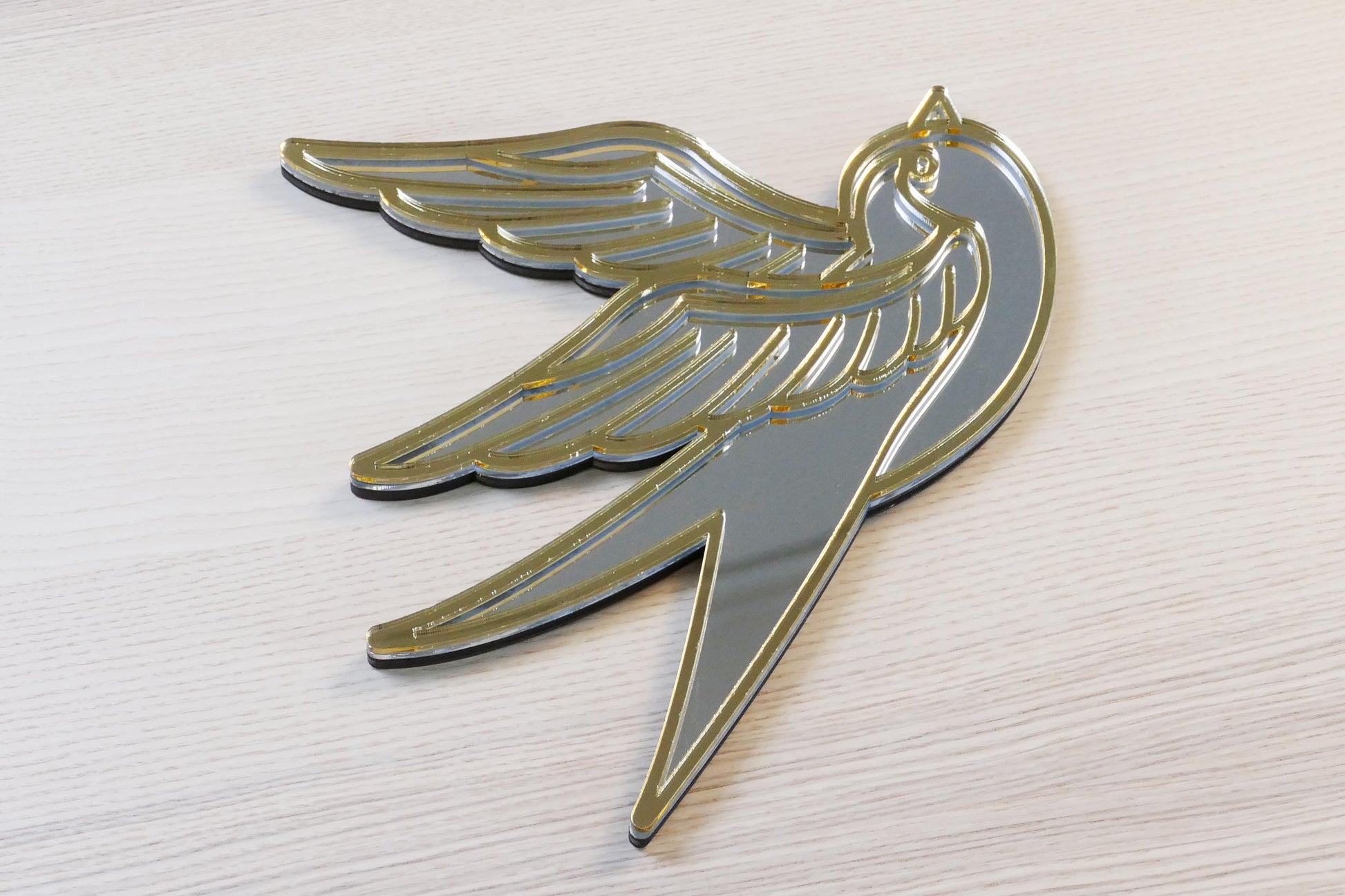 Gouden en zilveren acryl spiegel in tattoo-stijl van een zwaluw, hangend aan een muur. Tattoo Zwaluw Spiegel