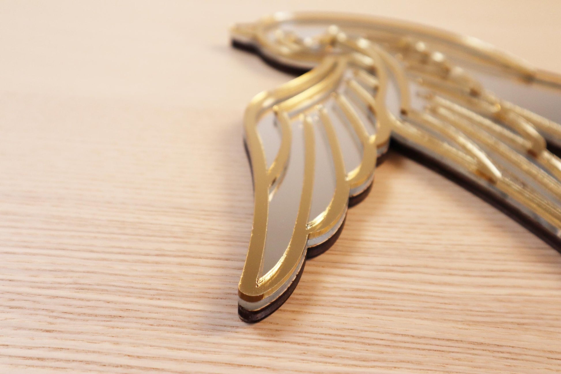 Gouden en zilveren acryl spiegel in tattoo-stijl van een zwaluw, hangend aan een muur.