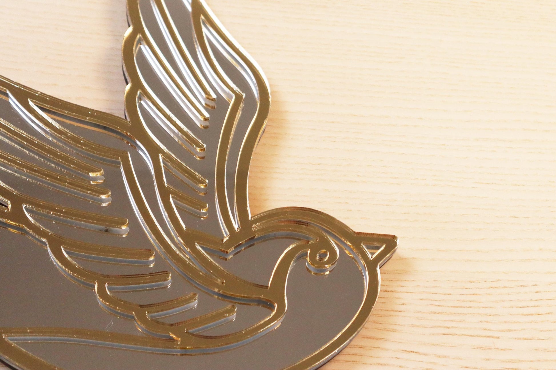 Gouden en zilveren acryl spiegel in tattoo-stijl van een zwaluw, hangend aan een muur. 